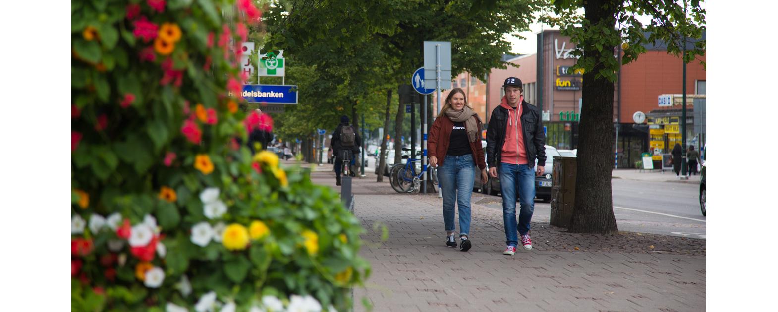 Two young people are walking on the sidewalk in the center of Kouvola