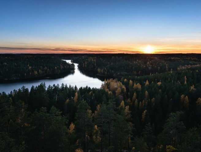 Ilmakuva Repoveden kansallispuistosta illan hämärässä. Edessä tummasävyistä metsää, keskellä vettä ja taivas on sinioranssi.