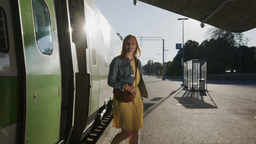 Nainen kesävaatteissa astuu junasta asemalaiturille.